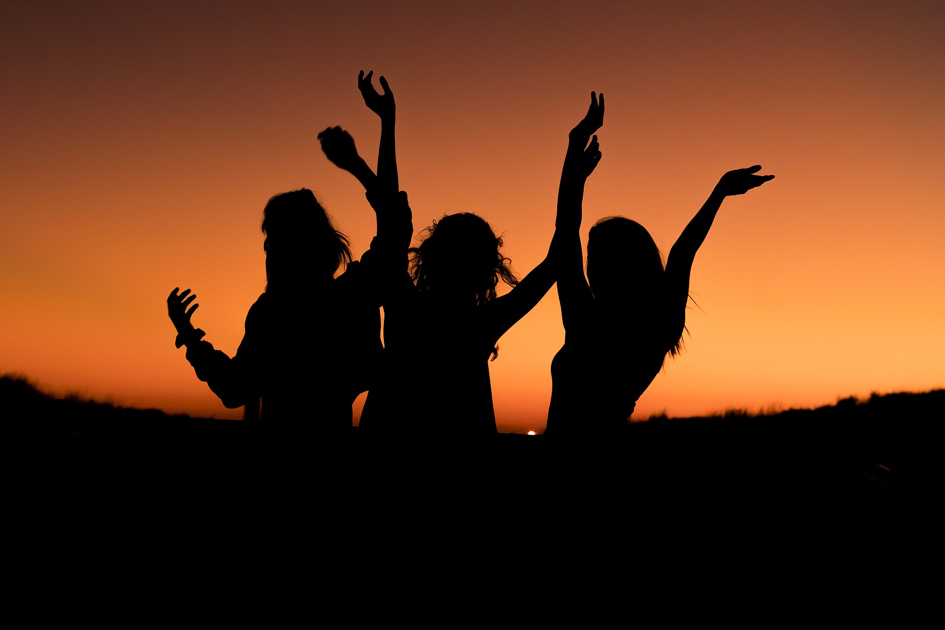 People raising their hands in joy at sunset